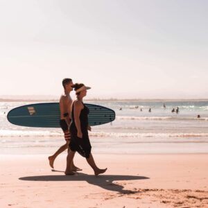 a man and a woman walking along a beach with a surfboard